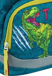 Teele Schulranzen mit einem grünen T-Rex-Graphic, roten Akzenten, Kratzspuren, gelbem Reißverschlussrand und einem grauen unteren Panel. Strapazierfähige Textur.