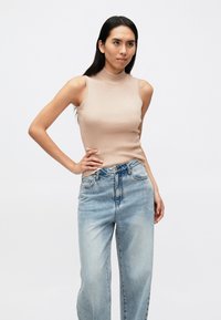 Bēšs, ribots bezroku tops ar augstu apkakli, kopā ar gaisā zilām, augsta vidukļa džinsiem, kuriem ir brīvs piegriezums un taisnas bikses kājas.