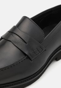 Sorte skinnloafers med en bred stropp over vampsen, med detaljerte sømmer og en teksturert gummisåle.