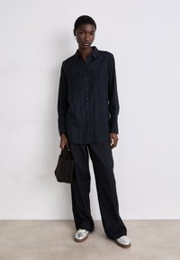Navy striped shirt with button front, two chest pockets, paired with matching wide-leg trousers and silver shoes. Soft brown textured bag.