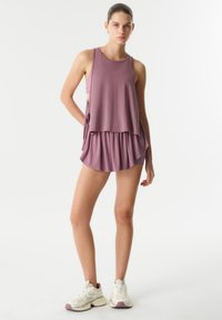 Top deportivo morado de corte holgado, combinado con una falda a juego. Presenta una tela suave y lazos laterales. Se lleva con zapatillas blancas y moradas.