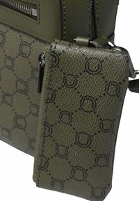 Sac à main vert olive avec une texture granuleuse et un motif circulaire noir. Comprend une fermeture éclair et un porte-monnaie détachable. Design lisse et élégant.