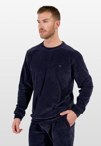 Granatowa koszula na długi rękaw z sztruksu o prążkowanej fakturze i okrągłym dekolcie. Na piersi znajduje się subtelne logo, w zestawie z dopasowanymi spodniami.