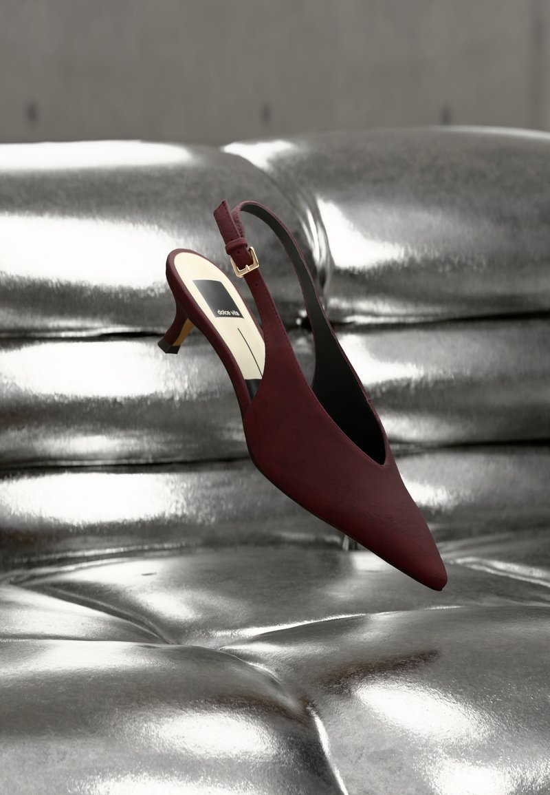 Σκούρο κόκκινο γόβα slingback με τακούνι kitten και μυτερή μύτη, ακουμπισμένη σε μια γυαλιστερή ασημένια επιφάνεια από δερματίνη με κουμπιά.