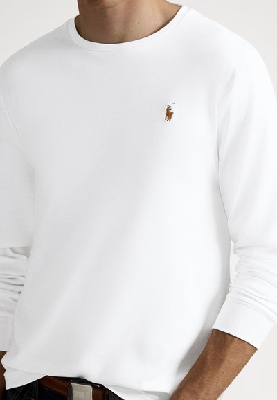 Fehér hosszú ujjú póló bordázott mandzsettákkal, a bal felső sarokban kis hímzett lóháton lovagló személy logóval.