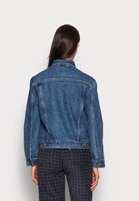 Vaalea sininen farkkutakki klassisella leikkauksella. Sisältää kaksi nappia vyötäröllä ja näkyvää ommelta. Takakatsauksessa näkyy jämäkkä muotoilu.