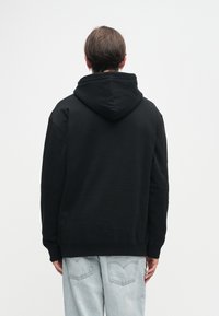 Melnas kapuce ar brīvu piegriezumu, ar ribotu apakšmalu un piedurknēm. Audums izskatās mīksts. Valkāta ar gaiši ziliem džinsiem.