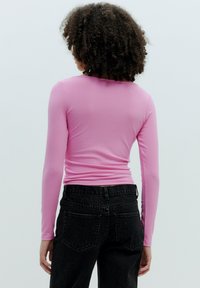 Langärmliges, geripptes rosa Oberteil mit tailliertem Schnitt, kombiniert mit hochgeschnittenen schwarzen Jeans. Glatte Textur und minimale Nähte.