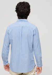 Lichtblauw langemouwen shirt met een button-down kraag, rugplooien en knoopsluitingdetails op de manchetten; gemaakt van een ademende, gestructureerde stof.
