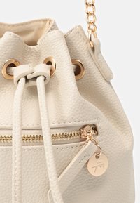 Borsa a secchiello in pelle effetto crema con chiusura a coulisse, tasca con zip dorata e dettaglio della tracolla in catena dorata.