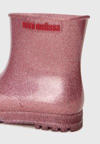 Blizgus rožinis guminis lietaus botas su blizgučiais. Yra raudona „mini melissa“ ženklinimas ir tekstūruota padas, užtikrinantis sukibimą.