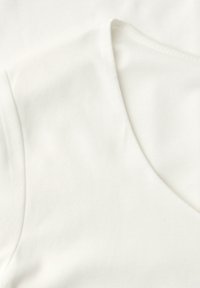 Gros plan sur un tissu blanc montrant une section pliée avec des coutures visibles et une texture douce.