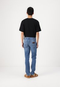 Camiseta negra de manga corta, jeans de mezclilla azul claro y zapatos marrones sin cordones. Los jeans tienen bolsillos traseros y una etiqueta de cuero marrón.