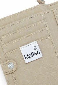 Beige textuur stof portemonnee sectie met meerdere kaartsleuven, een metalen drukknoop en een wit Kipling RFID veilige label.