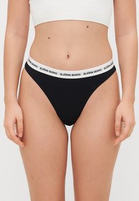 Černá tanga s bílým elastickým páskem, na kterém je nápis "BJÖRN BORG." Hladká tkanina, minimalistický design, bez dalších vzorů.