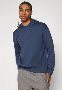 Námornícky modrá mikina vyrobená z mäkkého materiálu s kloktacou kapsou a rebrovaným lemom. Obsahuje vyšívané logo Calvin Klein na hrudi.