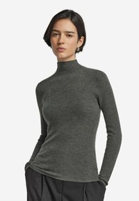 Ripp pullover mit hohem Kragen in dunkelgrau. Figurbetontes Design mit langen Ärmeln, weichem Material und subtiler Glanz. Kombiniert mit schwarzen Hosen.