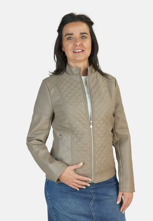 Chaqueta de cuero sintético color beige con un patrón acolchado en los hombros, cuello alzado y cierre de cremallera, combinada con una falda de mezclilla azul.