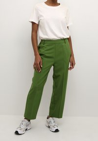 Pantaloni verdi su misura con vita alta e gambe dritti, abbinati a una t-shirt bianca a collo rotondo e scarpe da corsa argentate.