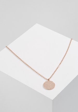 Collier délicat en chaîne or rose avec un pendentif rond présentant un motif géométrique texturé, exposé sur une surface blanche inclinée.