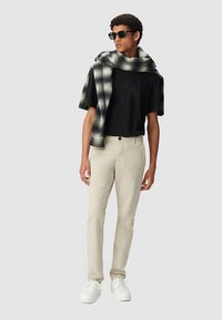 Czarny t-shirt z krótkim rękawem, beżowe spodnie, białe trampki oraz czarno-biała kraciasta szal wisząca na ramieniu.