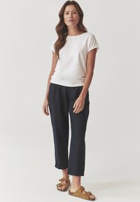 Witte top met korte mouwen en een ronde hals, gecombineerd met navy blauwe cropped broek. Tan instappers met een strikdetail.