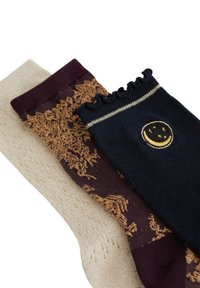 Tre par strømper: beige med et struktureret mønster, burgunder med guld accenter og marineblå med en bølget kant og en gul broderet smiley.