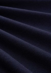 Dunkelblauem Stoff mit weicher Textur und subtilen Falten, die diagonale Schatten und Tiefe erzeugen.