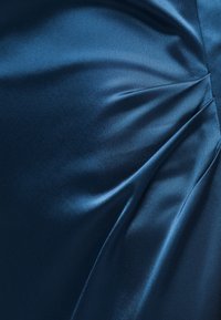 Υφασμα από μπλε σατέν με ομαλές πιέτες που δημιουργούν κυρτές πτυχώσεις και λεπτές αντανακλάσεις φωτός στην επιφάνεια.