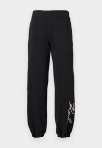 Svarte joggebukser med elastisk midje og mansjetter, prydet med en dekorativ brodert detalj i sølv og rødt på venstre ben.