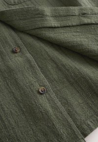 Close-up of textured dark green fabric with two brown buttons sewn on the material.