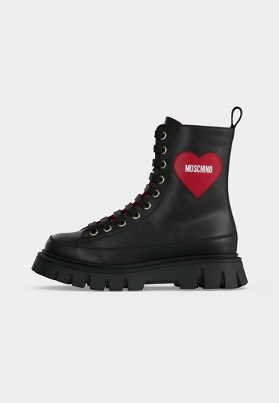 Botte de combat en cuir noir avec semelle épaisse, lacets à l’avant, patch cœur rouge avec le texte "Moschino" sur le côté, et languette à l’arrière.