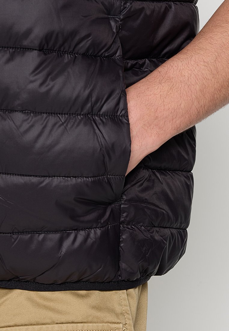 Schwarze gepolsterte Jacke mit horizontalen Nähten, ausgestattet mit einer Seitentasche und einer glatten, glänzenden Oberfläche. Texturiertes Material und ein taillierter Saum.