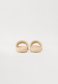 Sandales beiges avec une finition lisse et brillante, présentant un design simple à dos ouvert et une semelle intérieure moulée pour plus de confort. Semelles plates.