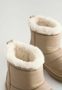 Stivali imbottiti beige con un morbido rivestimento in pelliccia sintetica bianca, caratterizzati da una superficie testurizzata e un tacco basso, progettati per comfort e calore.