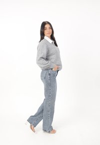 Grijze, textuurrijke trui met een V-hals en pofmouwen, gecombineerd met hoge, lichtblauwe denim jeans en doorzichtige hakken sandalen.