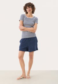 Chemise à manches courtes rayée en blanc et marine, associée à un short marine. Le short possède une taille élastique et des poches latérales.