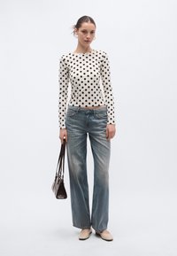 Pitkähihainen, kermanvärinen paita mustilla pilkuilla, yhdistetty vaaleansinisiin leveälahkeisiin farkkuihin ja beigen sävyisiin balleriinoihin; asusteena pieni ruskea käsilaukku.