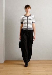 Cardigan à manches courtes rayé noir et blanc, boutonné à l'avant, associé à un pantalon noir ample et des chaussures noires. Design minimaliste.