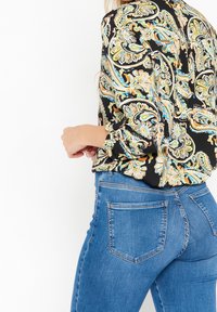 Svart blus med färggomt paisleymönster, långa ärmar och manschettdetaljer, i kombination med åtsittande blå denimjeans med bakfickor.