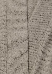 Gros plan d'un tissu beige tricoté montrant une texture côtelée détaillée et des points serrés et uniformes.