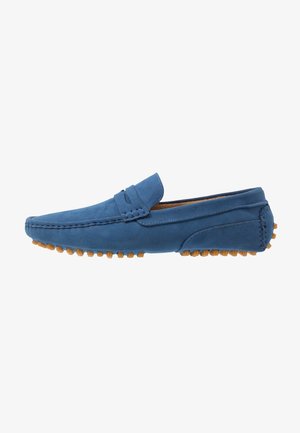 Chaussure mocassin en daim bleu avec une texture lisse, dotée d'une semelle en caoutchouc flexible avec de petits picots pour l'adhérence et le confort.
