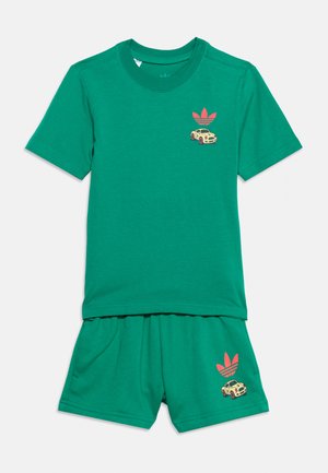 Rohelise lühikeste varrukatega T-särgi ja lühikeste pükste komplekt punase Adidas logo ja väikese beeži auto graafikuga rinnal ja lühikestes pükstes.