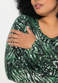 T-shirt à manches longues dans un motif abstrait vert et noir, avec un col rond et un tissu doux et texturé.