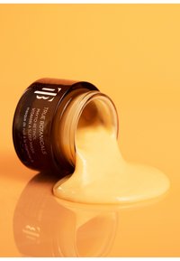 Brązowy szklany słoik z czarną pokrywką przewrócony, wylewający gęstą, kremową, żółtą maskę. Etykieta mówi "True Botanicals Phyto-Retinol Mask."