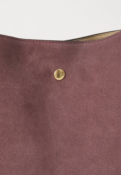 Borsa a tote in suede prugna con una texture liscia e senza motivi visibili, caratterizzata da un bottone rotondo d'oro e bordi cuciti.