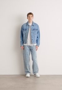 Light blue denim jacket over a white t-shirt, paired with light blue wide-leg jeans. White sneakers complete the outfit. Simple design, casual fit.