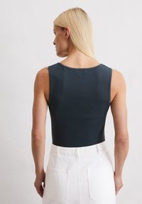 Geribbeld donkerblauw bodysuit met ronde hals, gecombineerd met een witte rok met hoge taille en grote achterzakken.