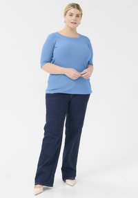 Top acanalado azul claro con mangas tres cuartos, combinado con jeans rectos azul oscuro y bailarinas beige de punta. Fondo liso.