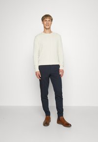 Krem pulover z pletenico, temno modri slim-fit hlače in rjavi usnjeni Chelsea škornji. Obleka vsebuje teksturirano blago in sproščen kroj.